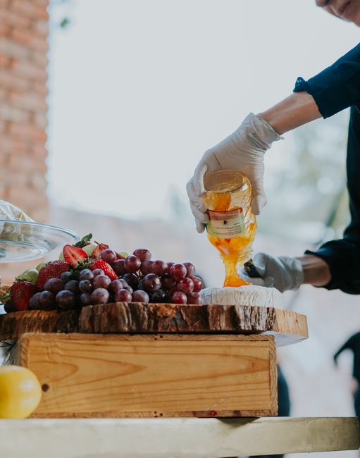 A person pours honey over cheese while preparing a fruit platter.