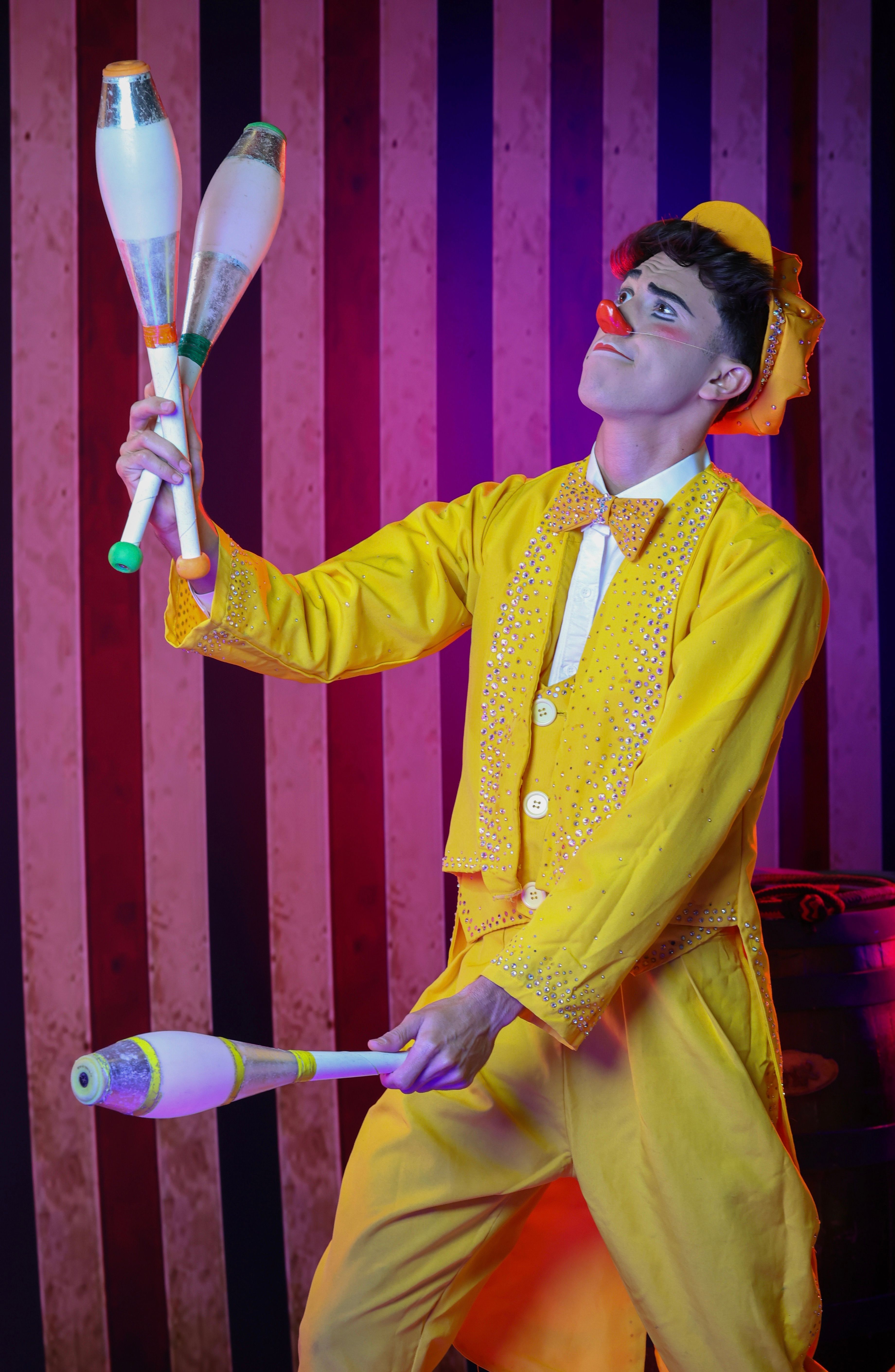 Colorful clown juggling on stage in bright yellow costume, entertaining audience.