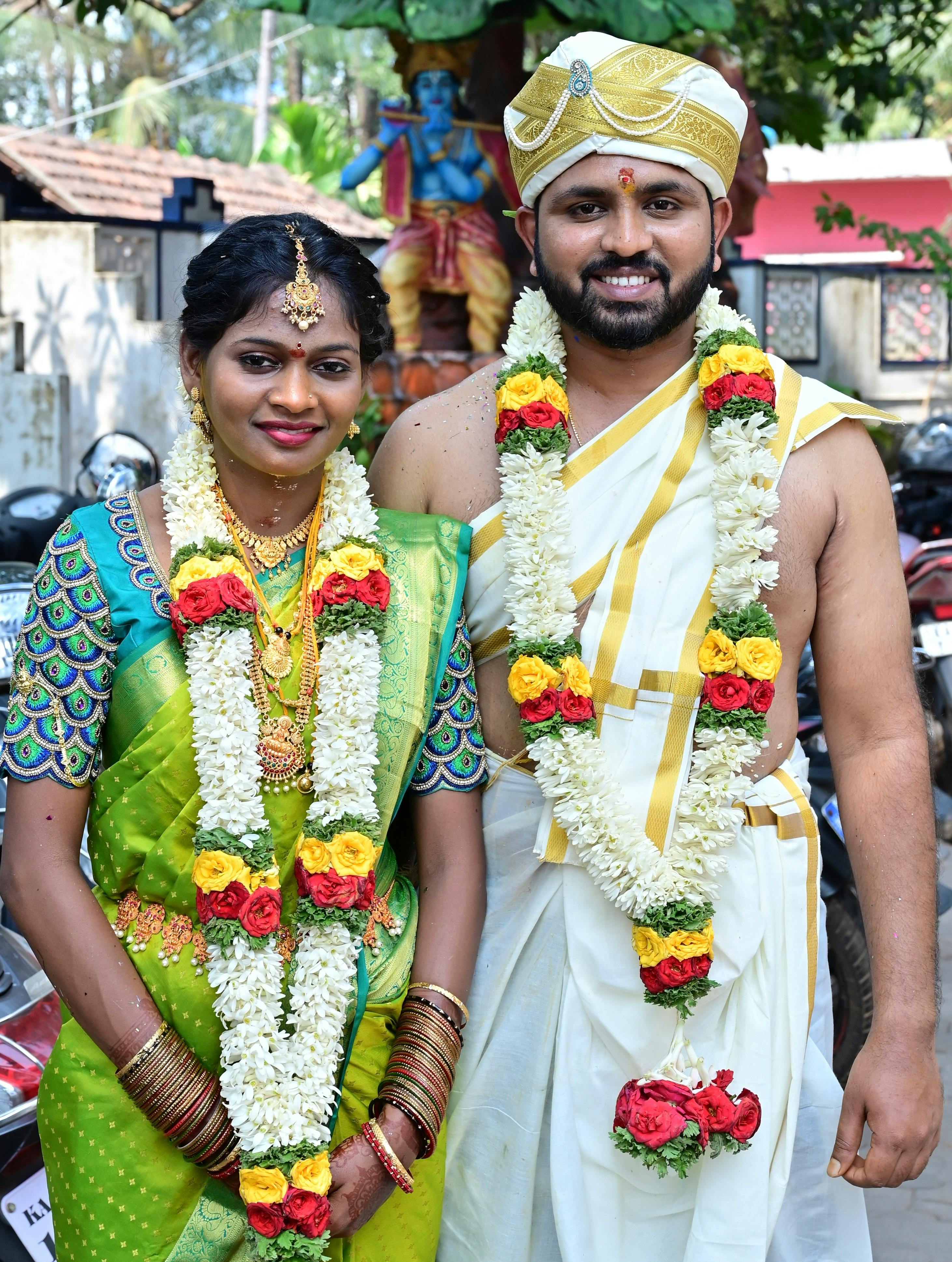 A happy South Indian couple in traditional wedding attire adorned with flower garlands.