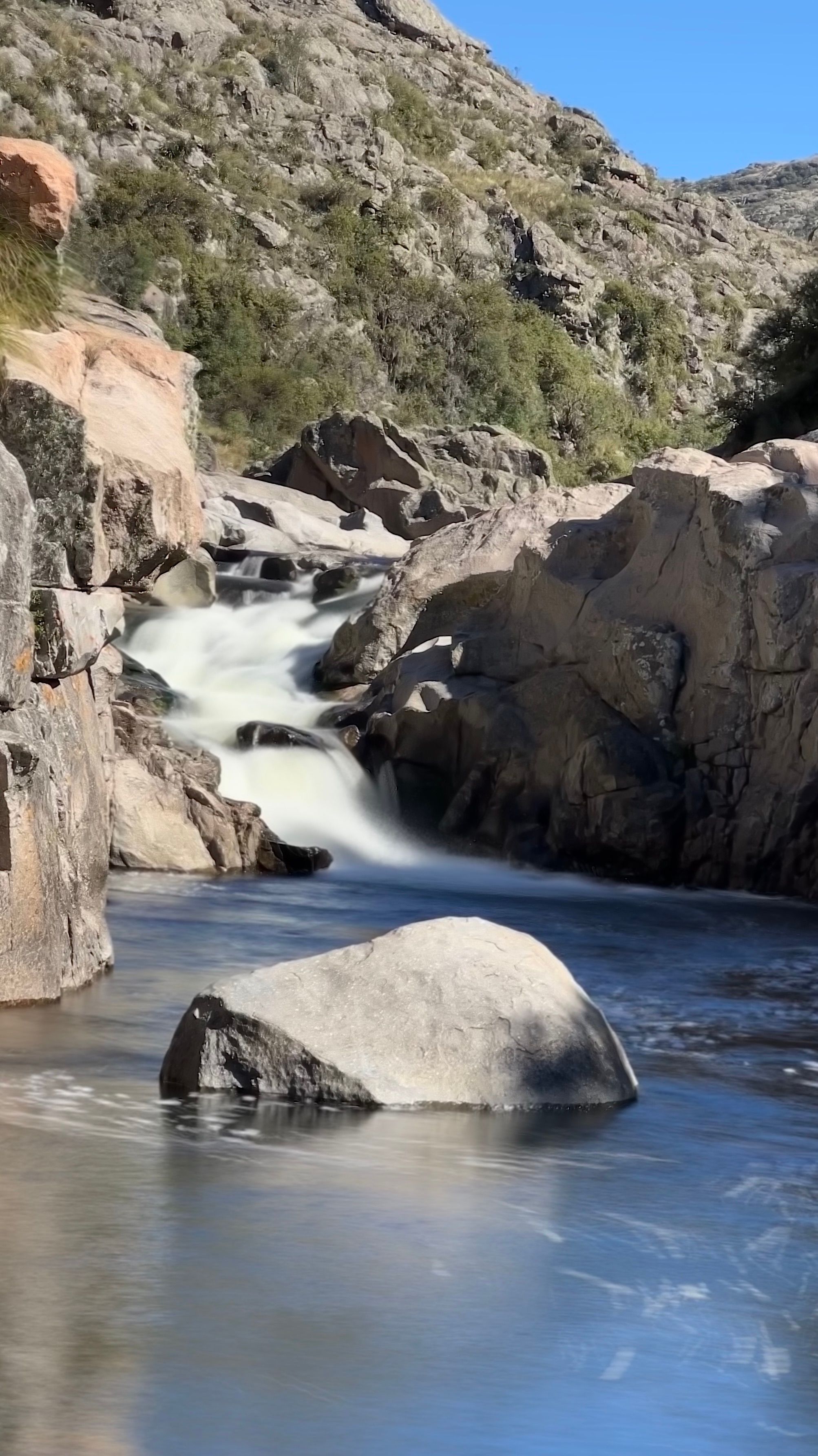 Tranquil waterfall cascading over rocks in Córdoba, Argentina with blue skies.