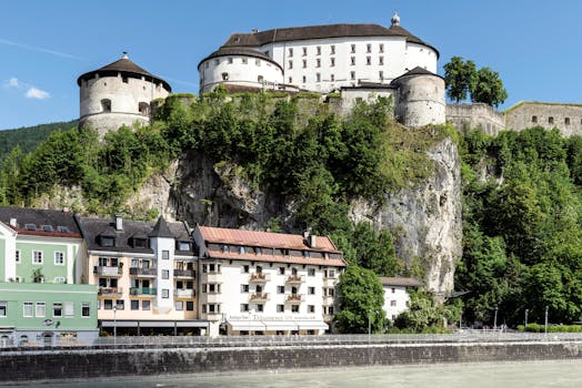 Scenic view of Kufstein Fortress above the River Inn, nestled in lush greenery.