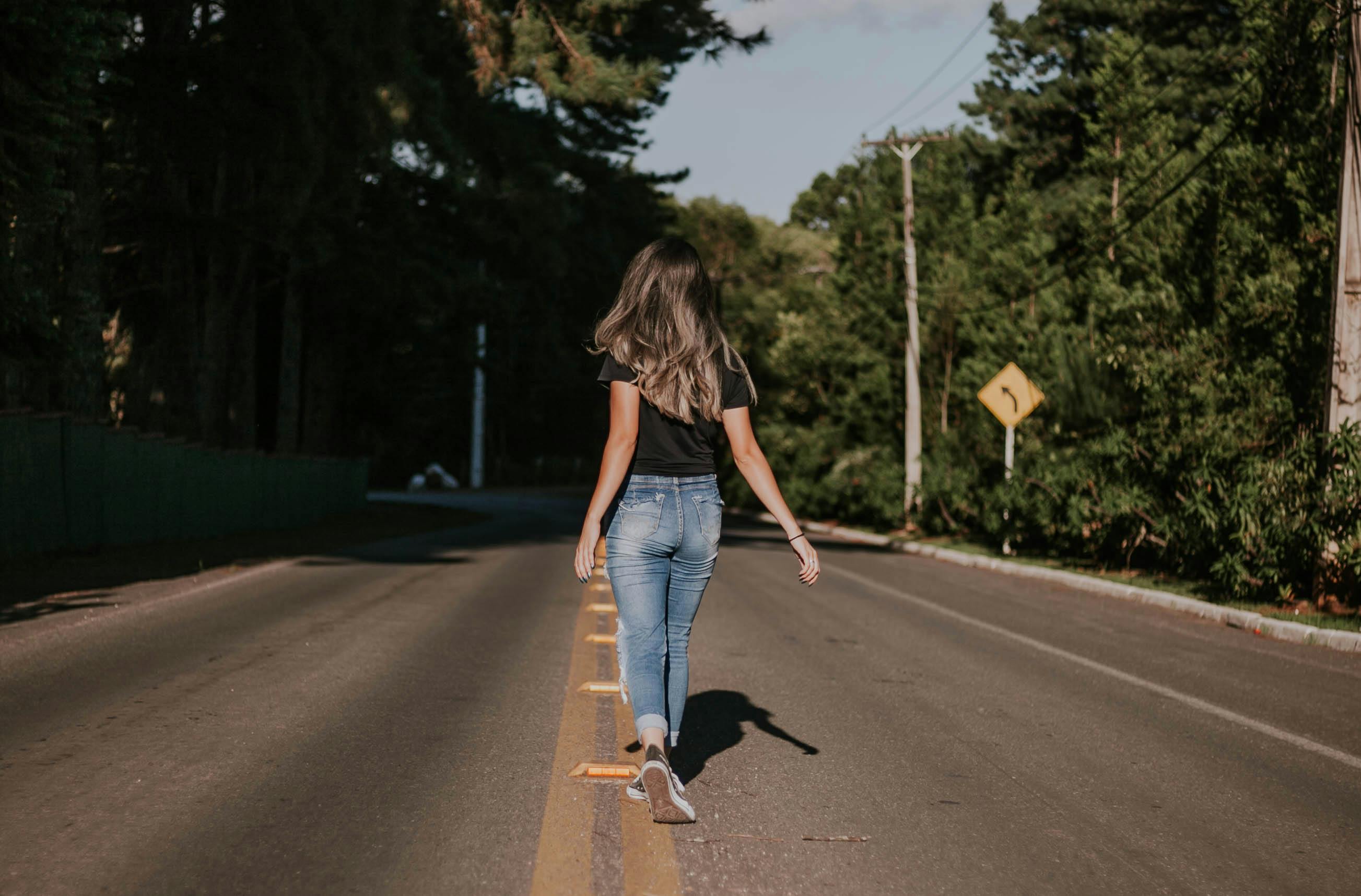 夏日里，一名女子悠闲地走在阳光明媚的林荫道上，这一幕被镜头从后方捕捉