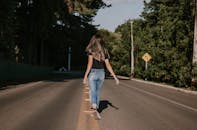 夏日里，一名女子悠闲地走在阳光明媚的林荫道上，这一幕被镜头从后方捕捉