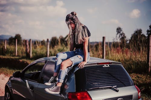 Woman Wearing Black Shirt And Blue Denim Jeans Sitting On Vehicle Roof