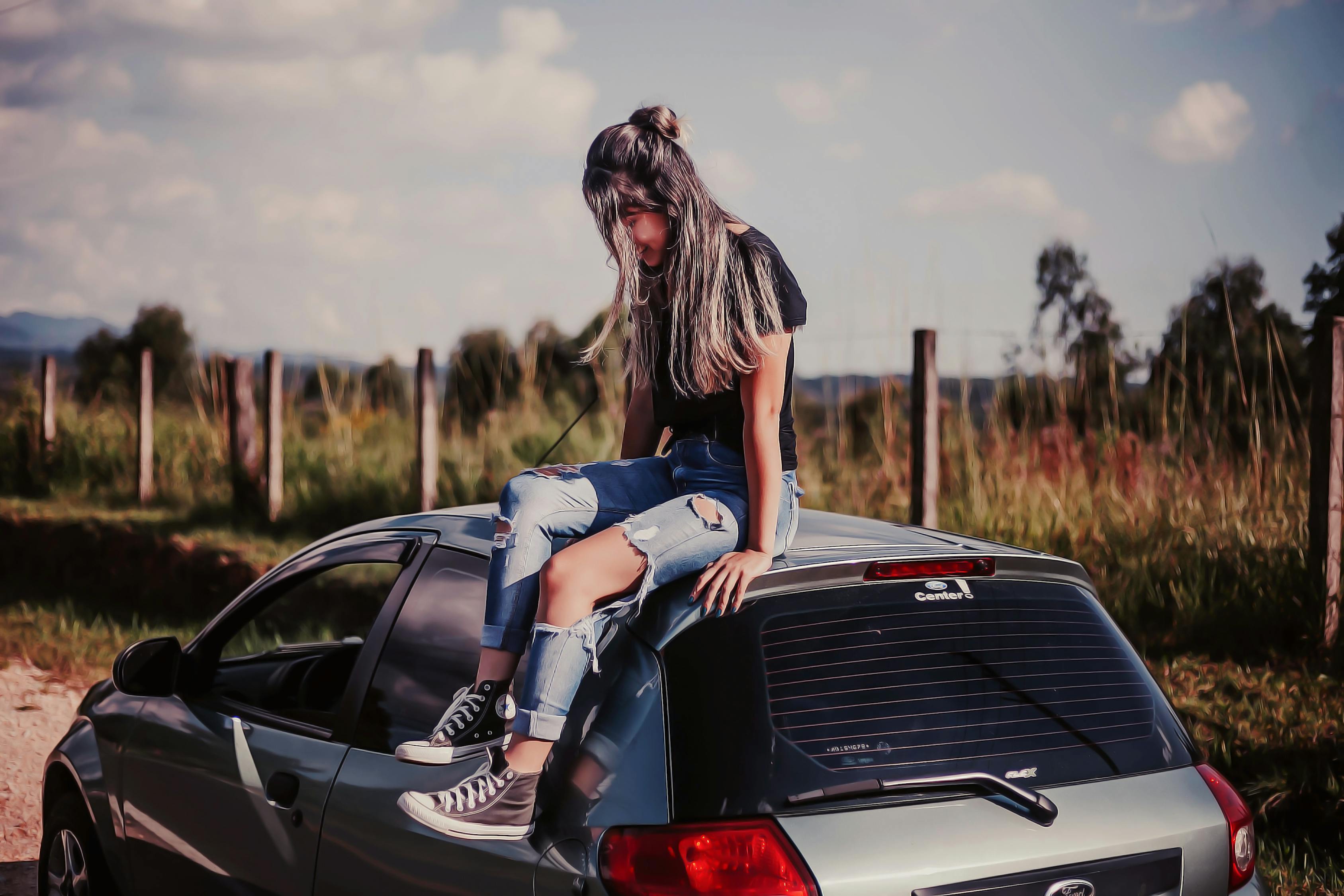 Woman Wearing Black Shirt And Blue Denim Jeans Sitting On Vehicle Roof ...