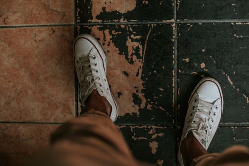 Free Top-down view of white sneakers on an aged tiled floor, displaying casual fashion against a rustic background. Stock Photo