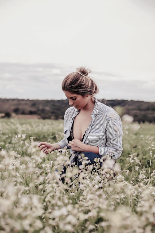 Photo of Woman With Opened Cleavage Knelling in the Middle of Grass Field