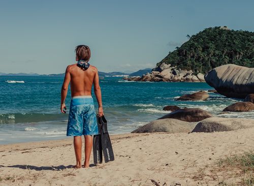 Free Young man with snorkel gear stands on a tropical beach, ready for adventure. Stock Photo