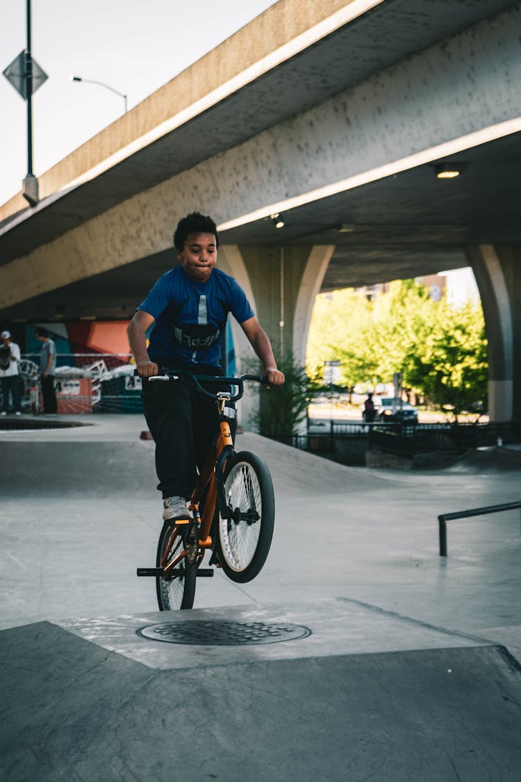 Boy In Blue Shirt Riding Bike On Ramp