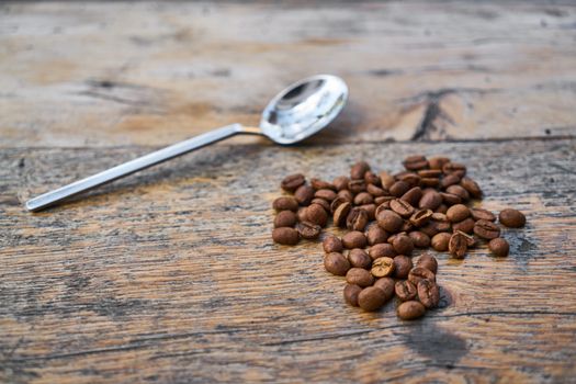 A close-up of roasted coffee beans and a spoon on a rustic wooden table.