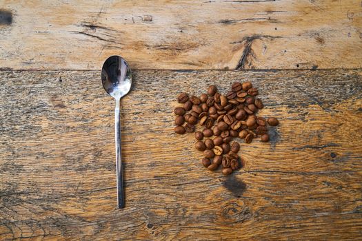 A flat lay of roasted coffee beans and a spoon on a rustic wooden table, showcasing coffee's aromatic appeal.