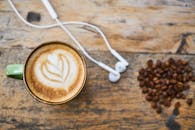 质朴的木桌上，一杯拿铁咖啡旁放着耳机和咖啡豆，泡沫拉花很巧妙