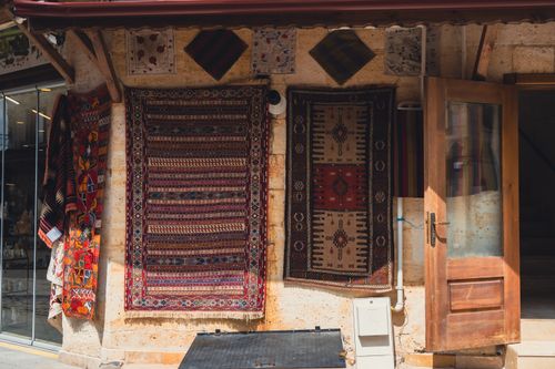 Free Handmade carpets hanging on an outdoor wall beside an open wooden door. A showcase of traditional craftsmanship. Stock Photo