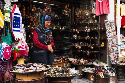 Elderly woman in hijab selling goods at a traditional Turkish bazaar.