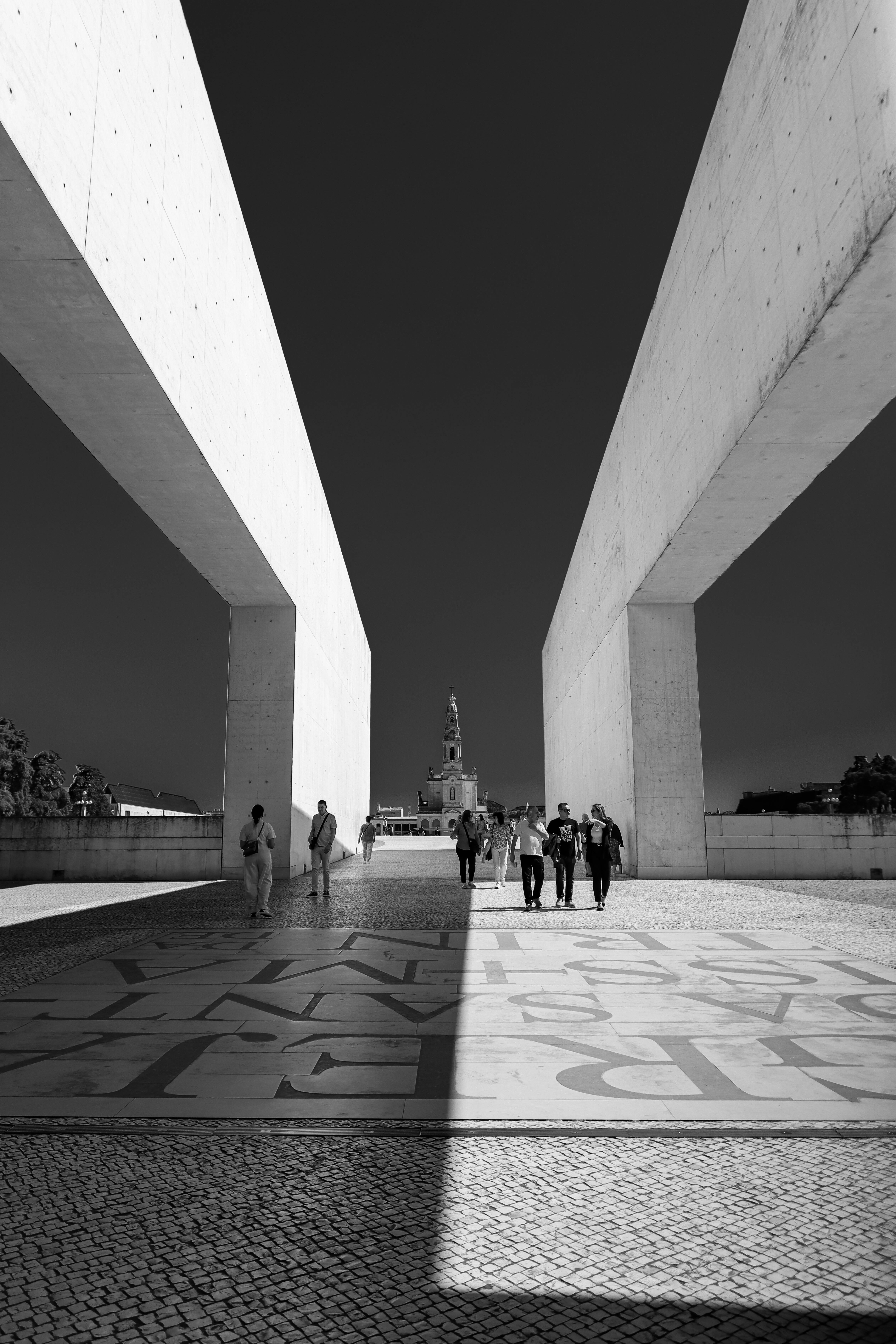 Black and white photo of pedestrians walking at Fátima Sanctuary's modern architecture in Portugal.