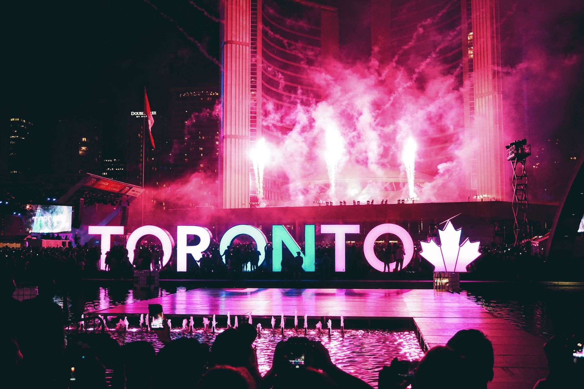 Toronto skyline beside a crowded transit platform, fans carrying national flags before kickoff
