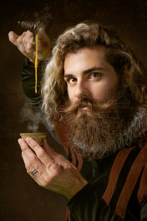 Free Majestic bearded man in costume elegantly pouring honey into a steaming cup against a dark backdrop. Stock Photo