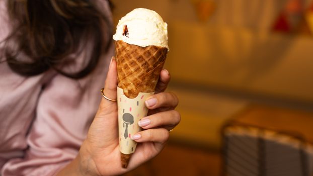 Hand holding an ice cream cone with vanilla scoop indoors. Perfect for dessert themes.