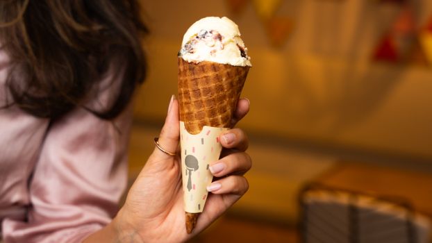 Close-up of a hand holding a delicious ice cream cone indoors.