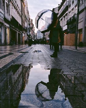 城市街道的水坑倒映着建筑物的影子，人们撑着雨伞行走其间