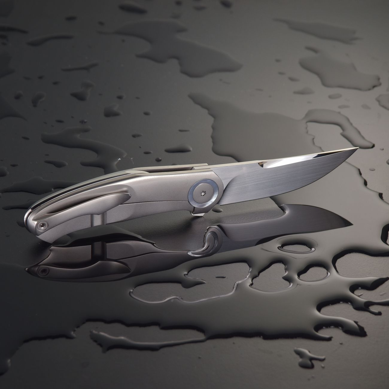 Close-up of a sleek pocket knife on a wet surface, showcasing sharpness and stainless steel design.