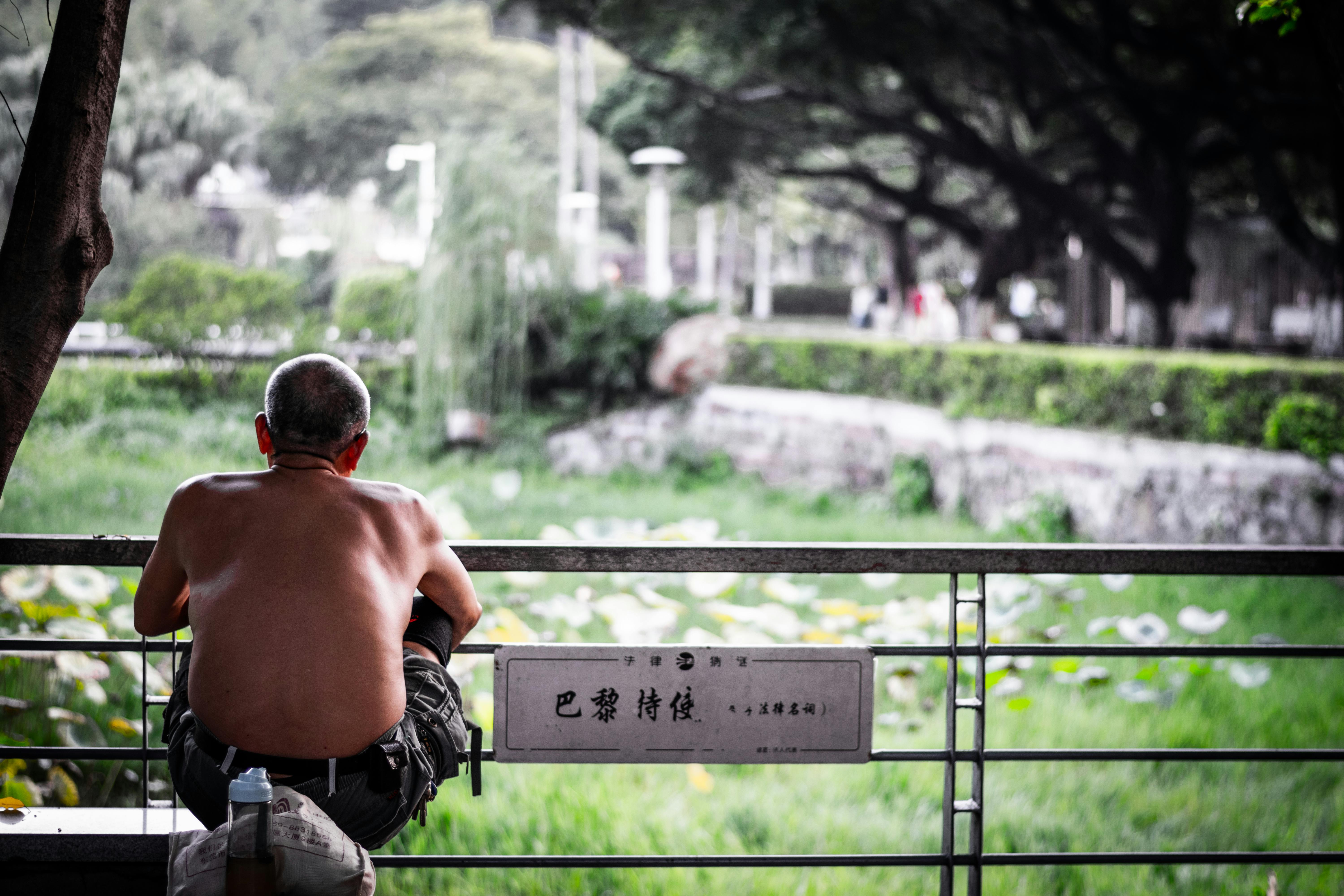 Shirtless man enjoying a peaceful moment by a pond in a lush park setting.
