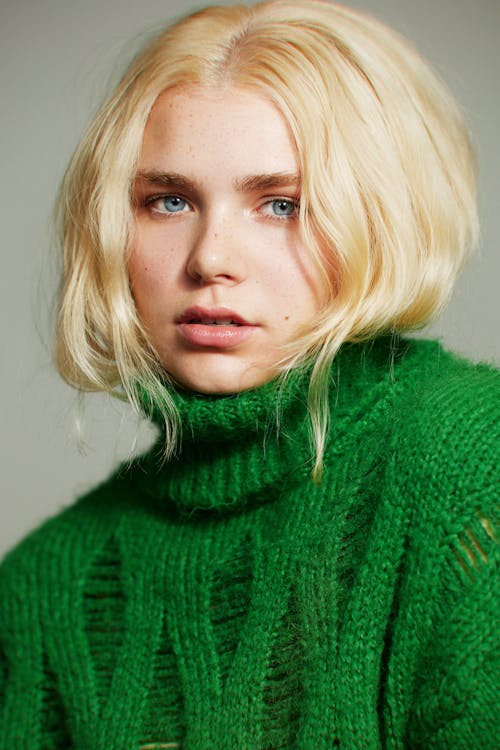 A blonde woman with blue eyes wearing a green sweater