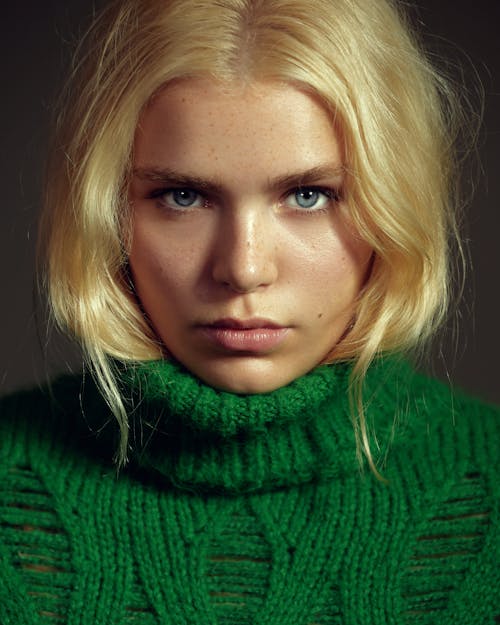 A blonde woman with blue eyes wearing a green sweater