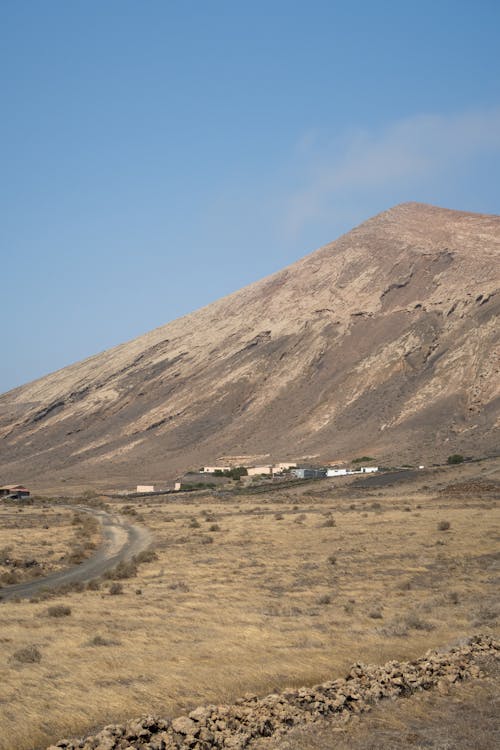 A mountain with a dirt road and a house in the distance