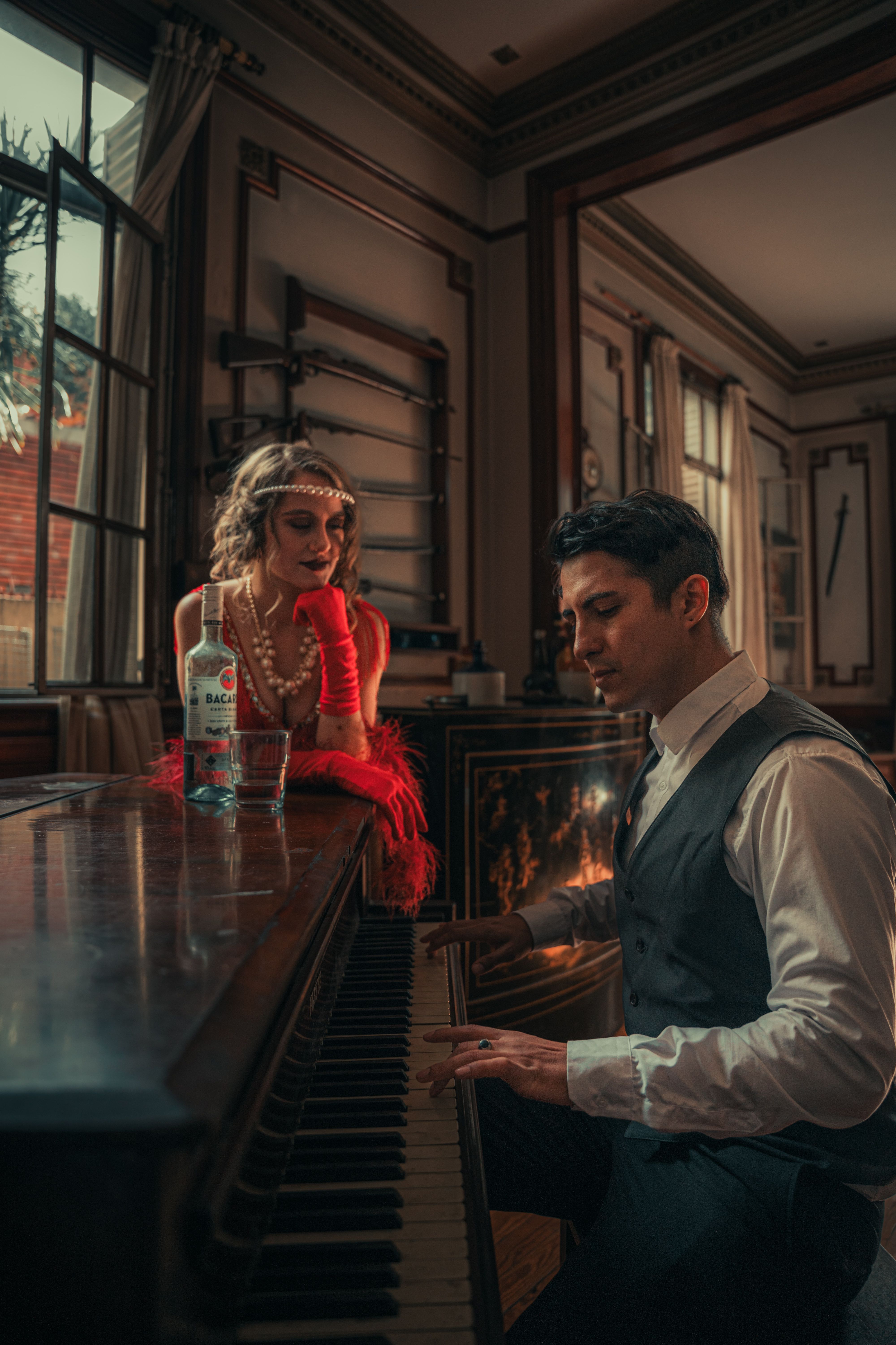 1920s style scene with actors and costumes around a piano, indoors.
