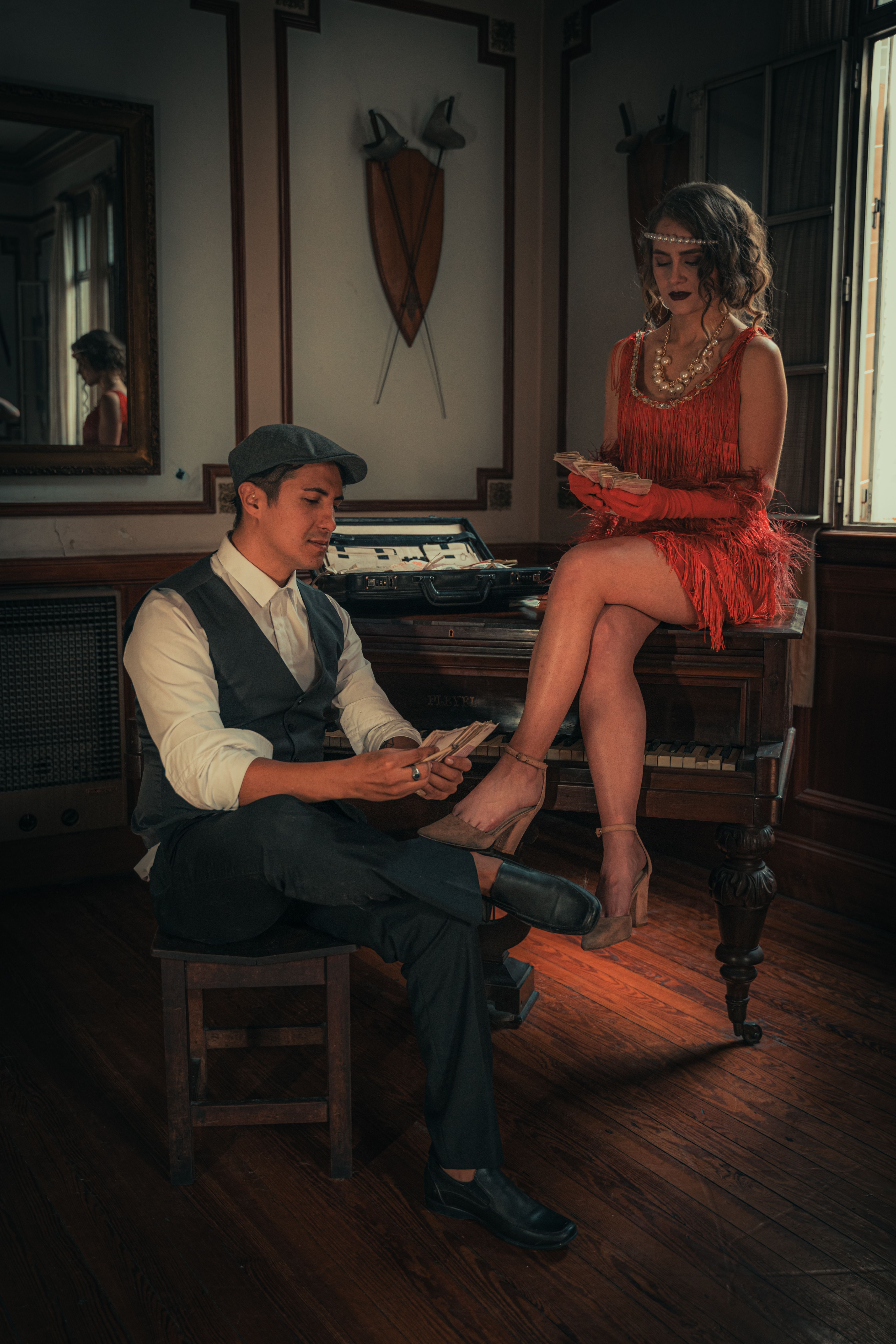 A stylish couple in vintage attire count money near a retro piano, evoking a 1920s Gatsby vibe.