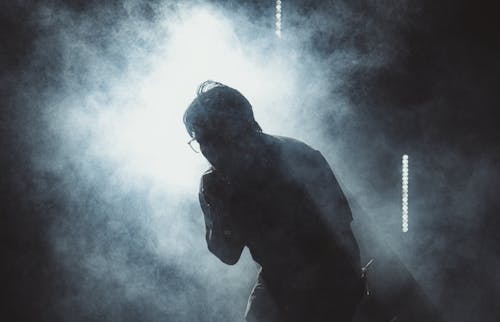 A man is silhouetted in smoke with a microphone