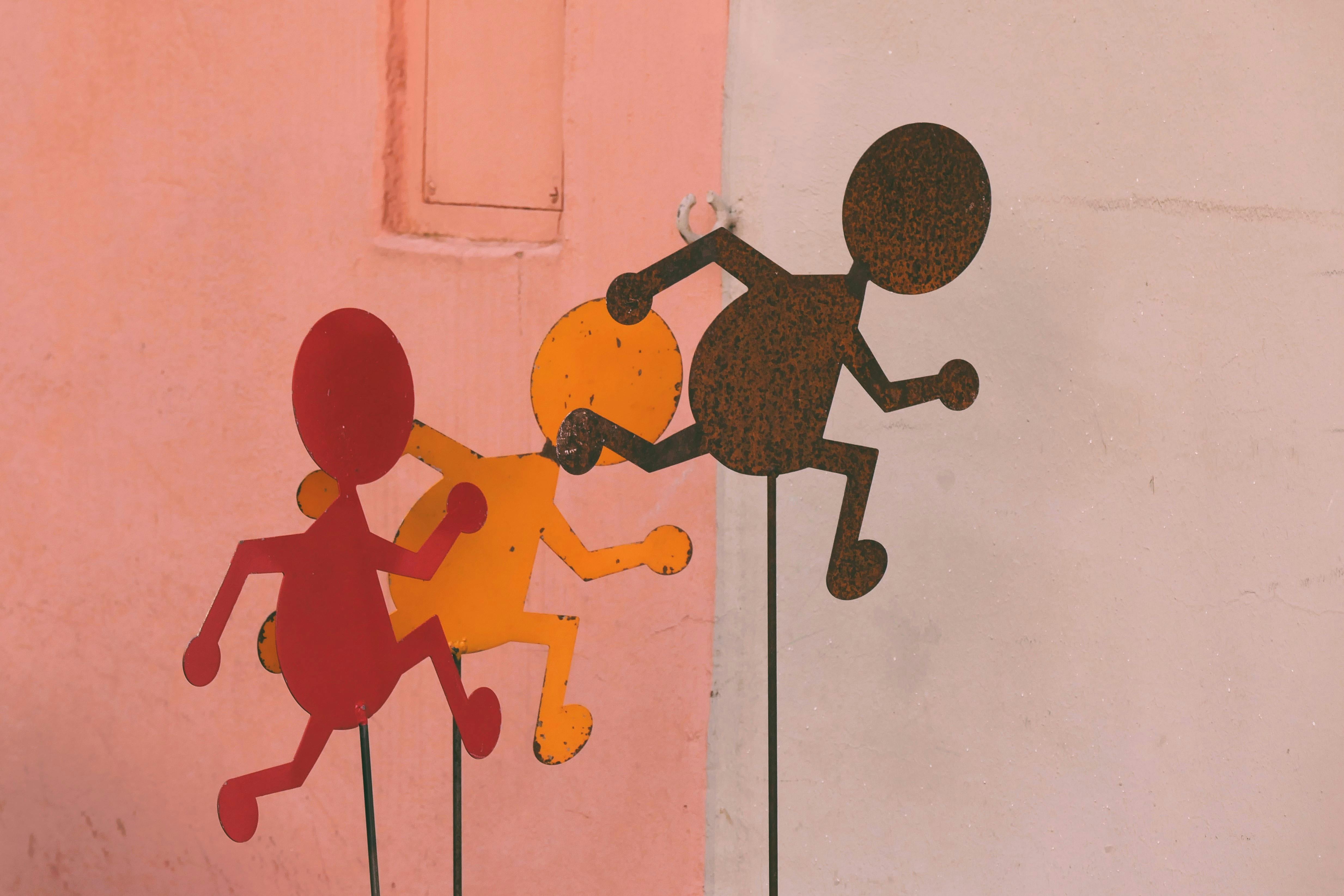 metal anthropomorphic figurines on sticks against a pink wall