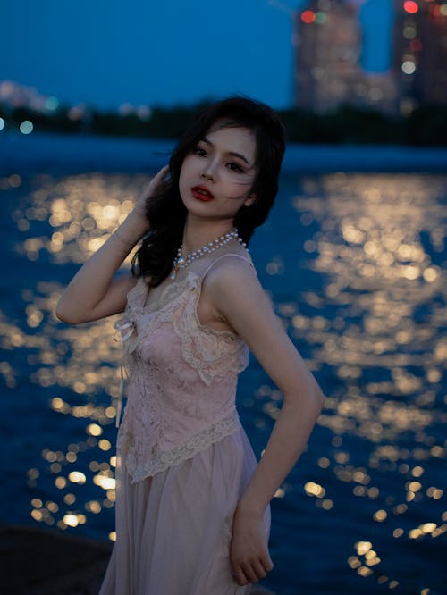 A woman in a pink dress posing by the water