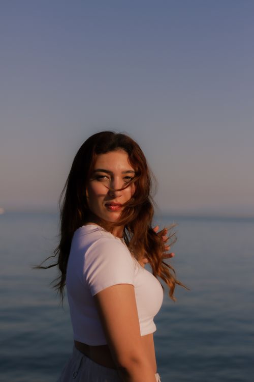 Free Young woman in a crop top enjoys a peaceful sunset by the sea, experiencing tranquility and warmth. Stock Photo