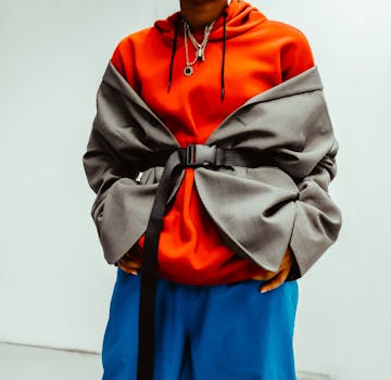 Stylish urban fashion outfit featuring a red hoodie, grey jacket, and blue pants. Trendy and modern look.