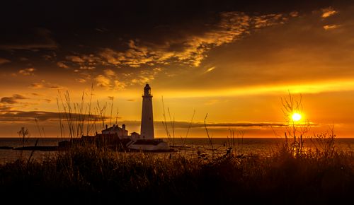 Free A serene view of a lighthouse against a vibrant sunset on a coastal island. Stock Photo