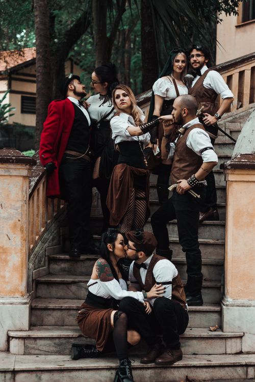 Free Group of adults in vintage steampunk attire gathered on stairs, creating a vibrant, eclectic scene. Stock Photo