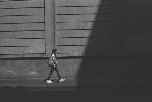 Free Monochrome image of a woman walking along a sunlit city sidewalk capturing urban solitude. Stock Photo