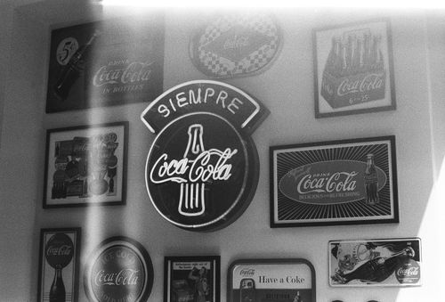 Free Black and white photo of vintage Coca-Cola signs and memorabilia on a wall. Stock Photo
