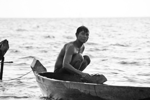 Free A contemplative fisherman sitting on a traditional wooden boat in black and white. Stock Photo