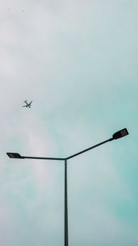 A scenic view of a plane flying above a city street lamp against a clear sky.