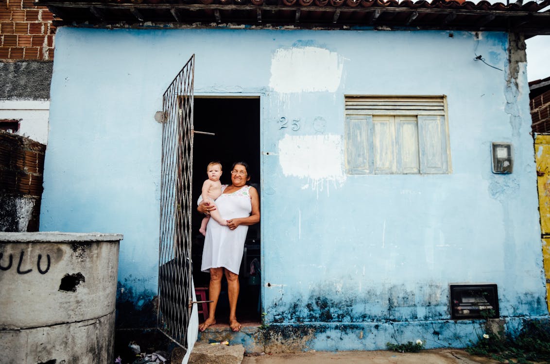 Woman Holding a Baby at Doorstep of Shabby House