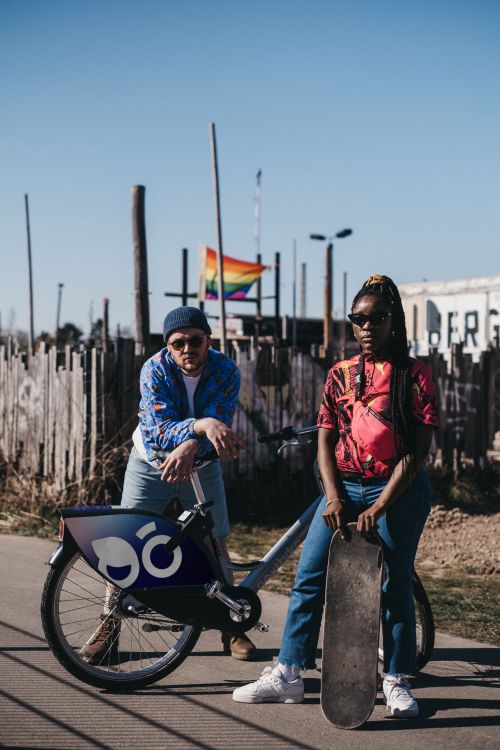 Free A man and woman with a bike and skateboard in a sunny city environment. Stock Photo