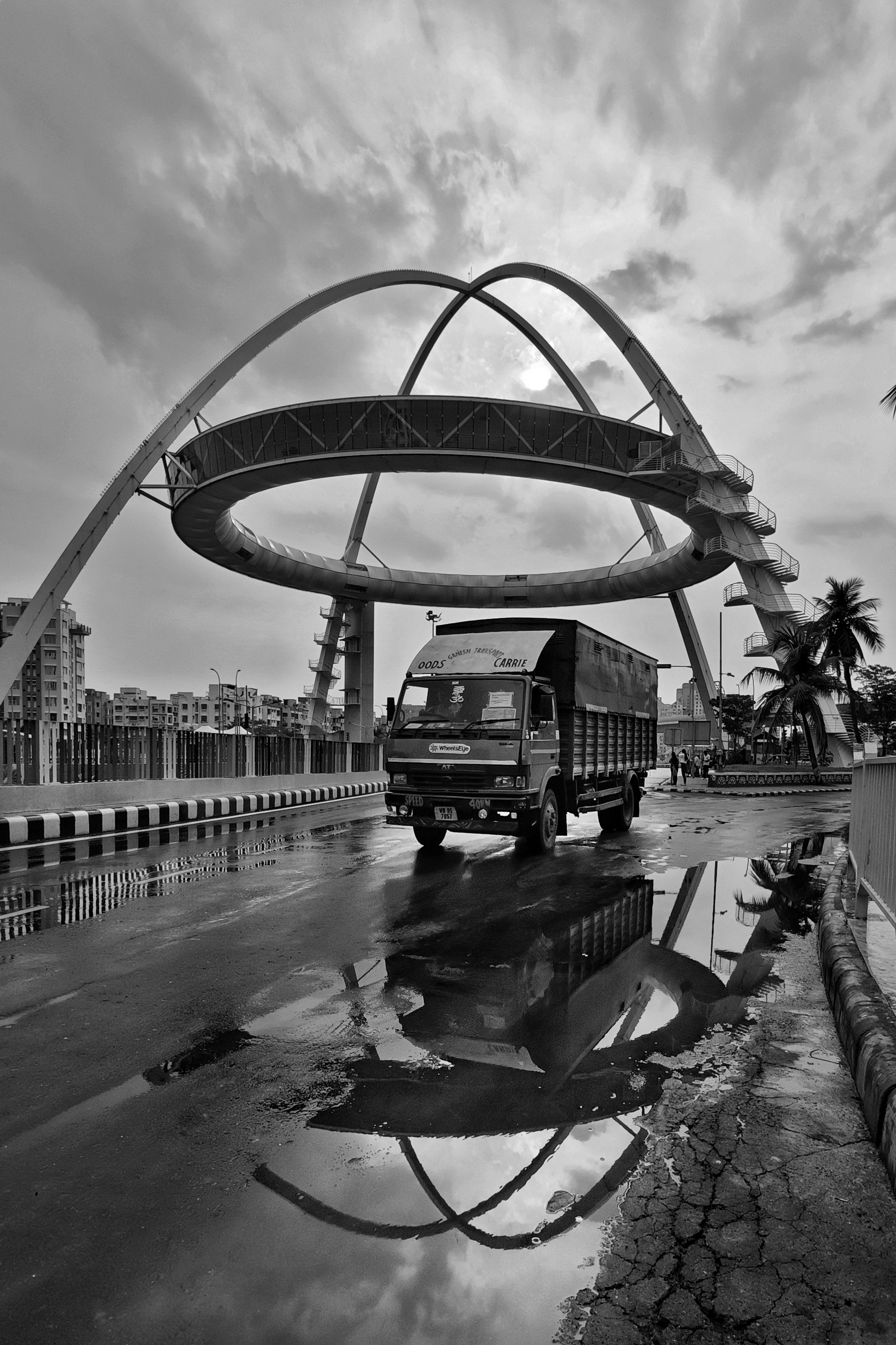 Black and white urban scene featuring a truck reflection at Biswa Bangla Gate, Kolkata.