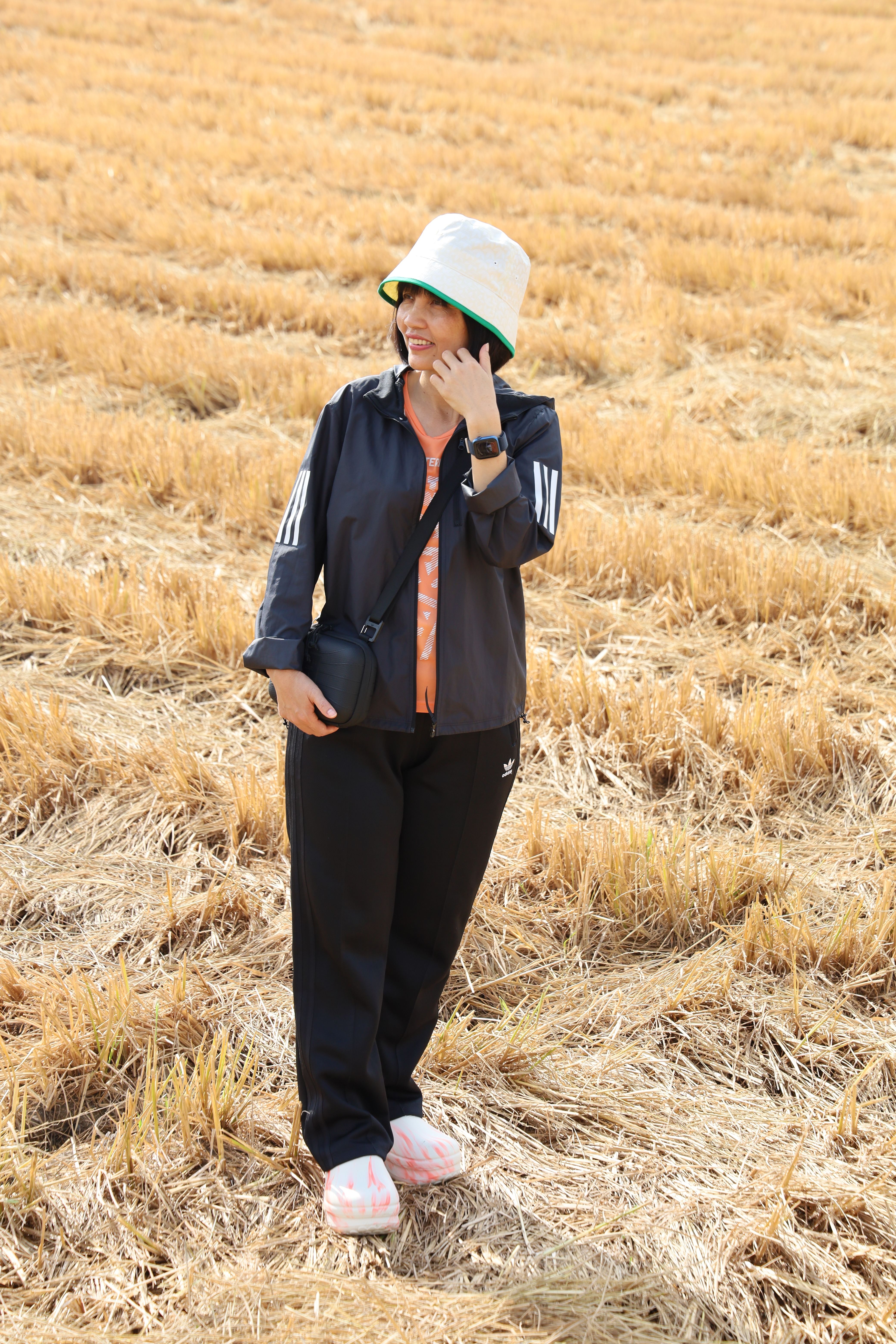Asian woman standing in a straw field during summer, wearing a casual outfit and summer hat.