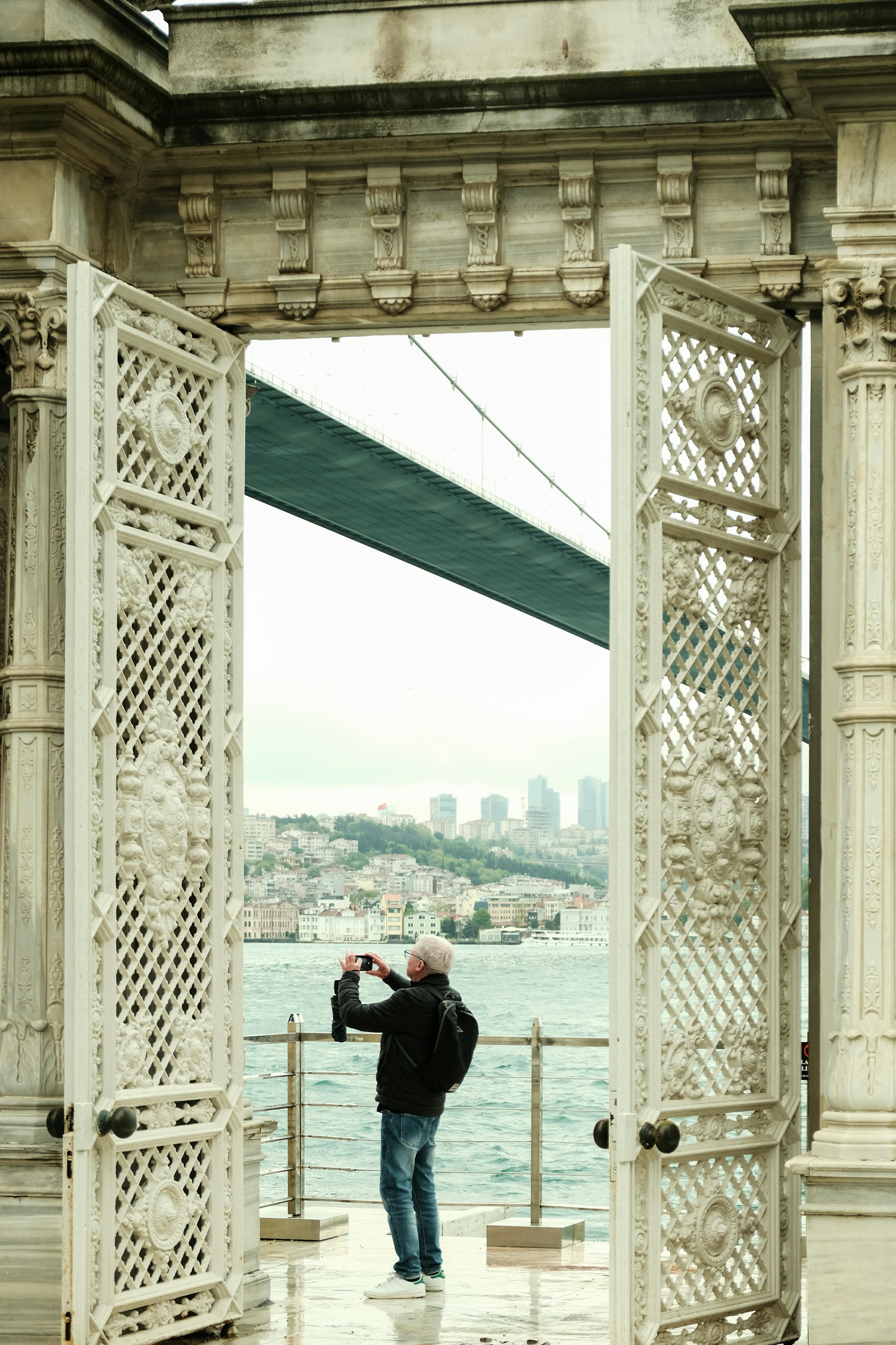 A man photographing Istanbul scenery through palace gates with Bosphorus view.