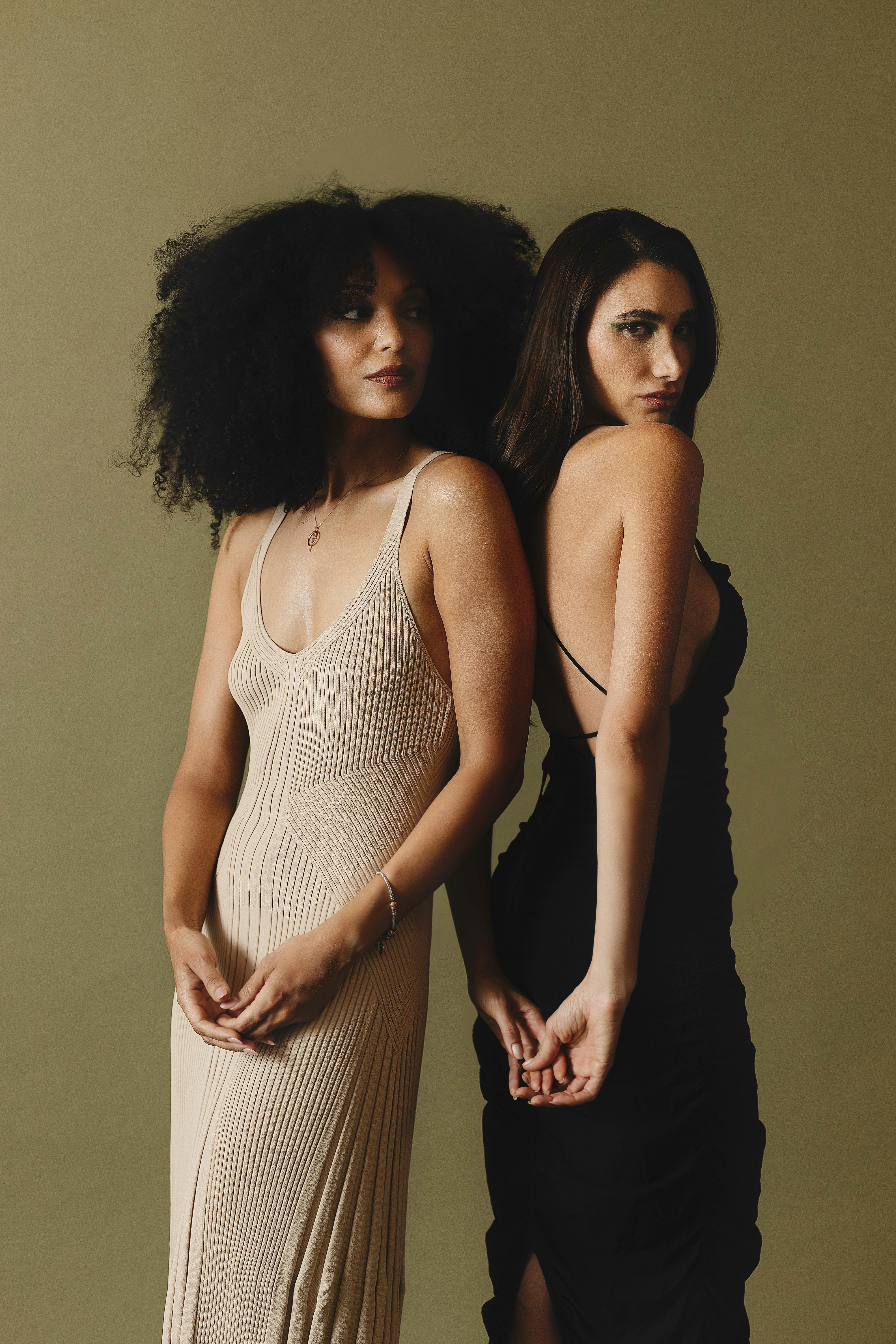 Stunning portrait of two women in elegant dresses standing together against a neutral backdrop.