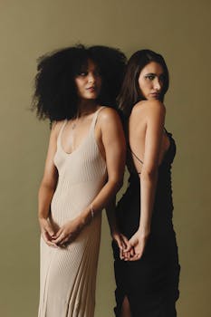 Stunning portrait of two women in elegant dresses standing together against a neutral backdrop.