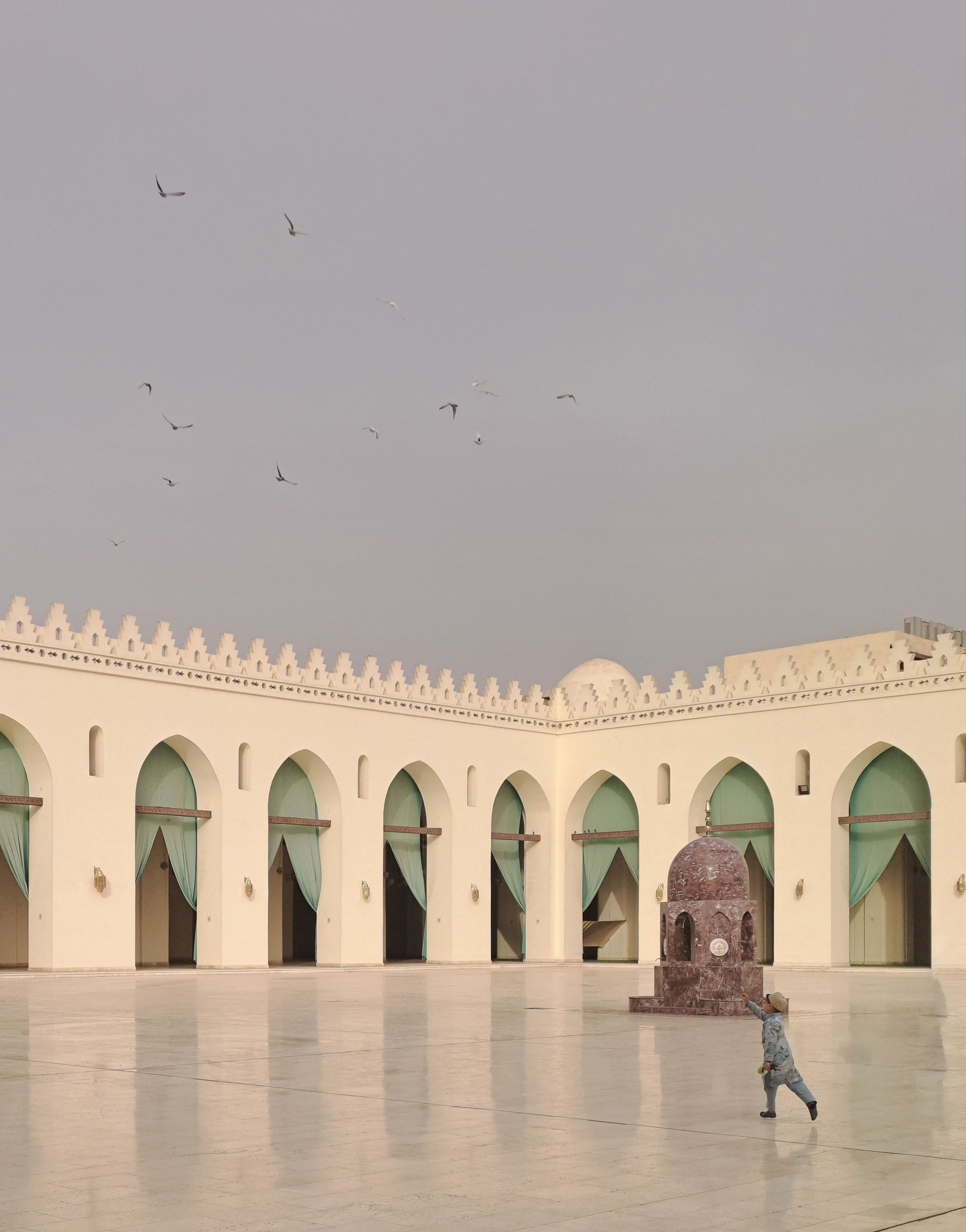 Peaceful courtyard of Al-Hakim Mosque in Cairo with arches and a lone figure.
